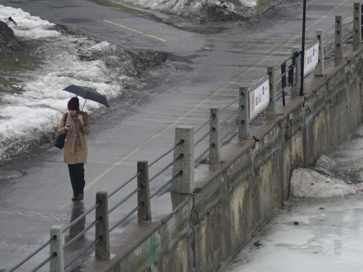 A person gripping an umbrella walks alongside the Rideau Canal on a sloppy winter day in March 2017.  (Giacomo Panico/CBC - image credit)