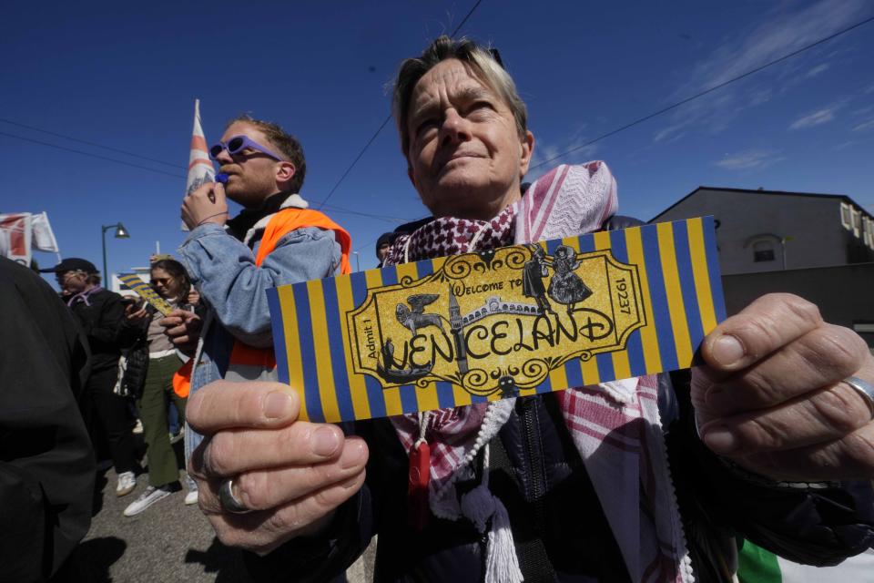 A citizen shows a ticket with the writing 'Veniceland' during a protest against Venice Tax Fee in Venice, Italy, Thursday, April 25, 2024. The fragile lagoon city of Venice begins a pilot program Thursday to charge daytrippers a 5 euro entry fee that authorities hope will discourage tourists from arriving on peak days. The daytripper tax is being tested on 29 days through July, mostly weekends and holidays starting with Italy's Liberation Day holiday Thursday. Officials expect some 10,000 people will pay the fee to access the city on the first day, downloading a QR code to prove their payment, while another 70,000 will receive exceptions, for example, because they work in Venice or live in the Veneto region. (AP Photo/Luca Bruno)