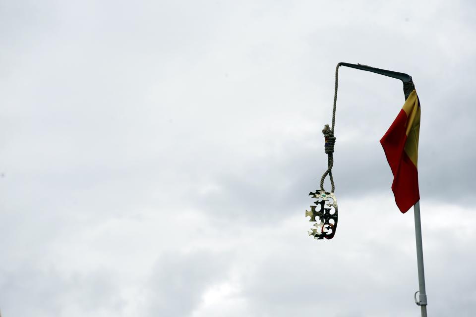 A crown hangs from a gallows beside a Spanish flag during the