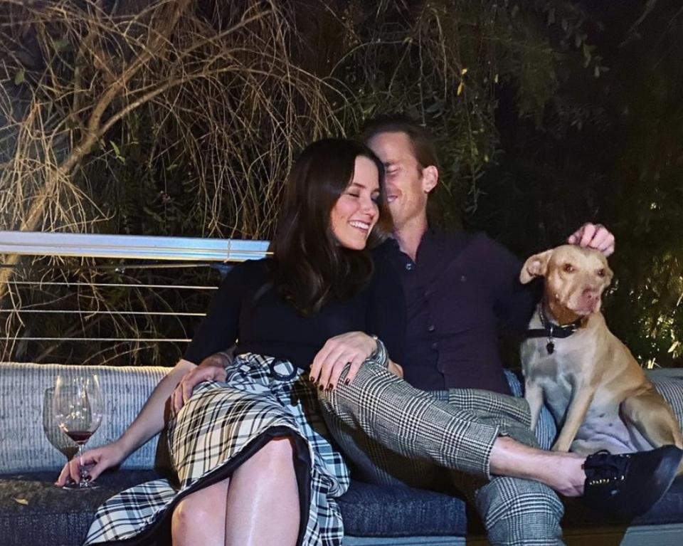 Sophia and Grant cozy up on a couch outside with a dog sitting nearby