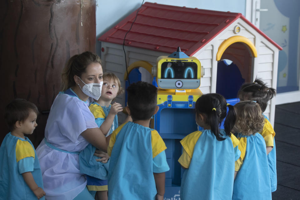 ARCHIVO - En esta imagen de archivo del viernes 4 de septiembre de 2020, una profesora muestra un robot que toma la temperatura a los niños y la muestra en una pantalla, en una escuela infantil de Madrid, España. Los alumnos de menos de tres años en la capital española acudían a la escuela el viernes, su primera actividad educativa presencial desde que comenzó una estricta cuarentena contra el coronavirus en marzo. (AP Foto/Paul White, Archivo)