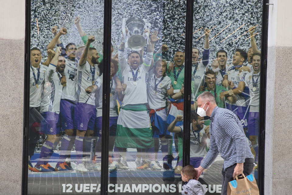 A man and a young boy walk past a Real Madrid poster of the team celebrating in a merchandising shop in Madrid, Spain, Monday, April 19, 2021. UEFA president Aleksander Ceferin says players at the 12 clubs setting up their own Super League could be banned from this year's European Championship and next year's World Cup. Ceferin spoke after a UEFA executive committee meeting held only hours of the English, Italian and Spanish clubs announced the project that threatens to split European soccer. (AP Photo/Paul White)