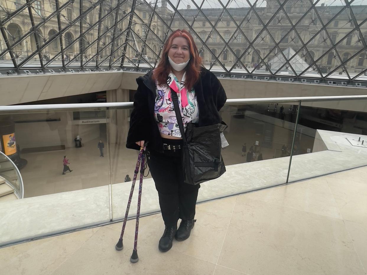 Ashley Couto with cane in Paris in front of glass