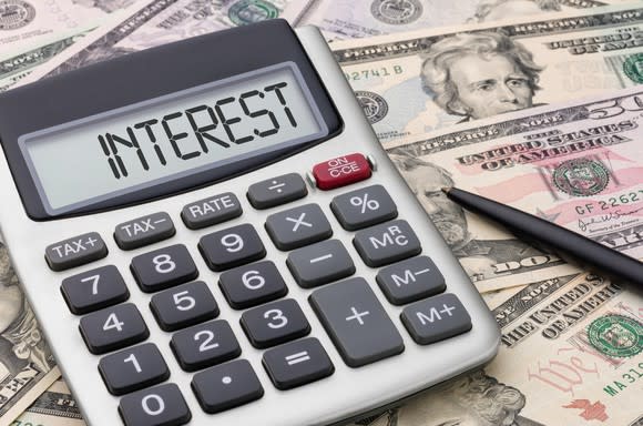 A calculator lying on a messy pile of cash, with the word interest written on the screen.