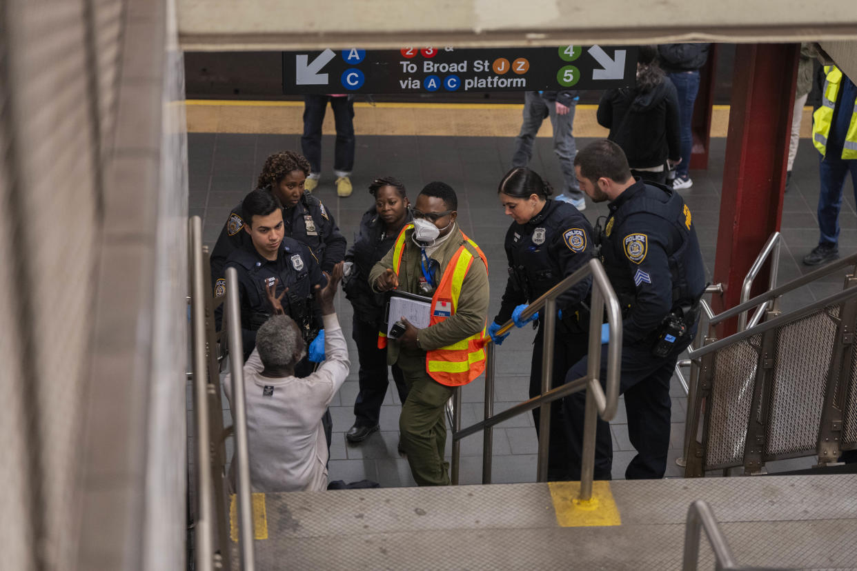 Ameed Ademolu, center, a nurse, with NYPD police officers, speak with a man at the Fulton Street subway station in Lower Manhattan on March 13, 2024. (Hiroko Masuike/The New York Times)
