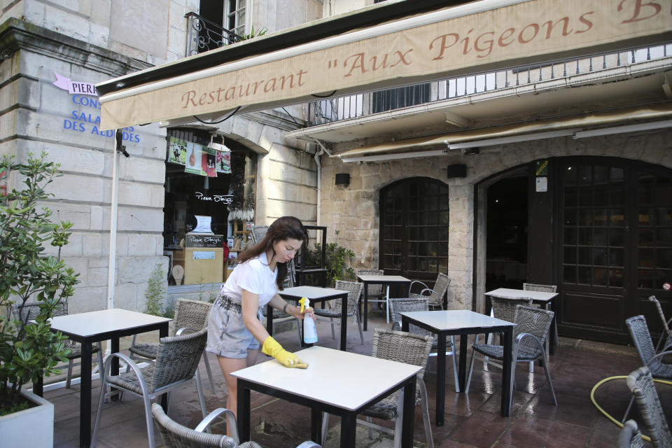 A restaurant employee Annabelle Mathis cleans a table in a restaurant of Saint-Jean-de-Luz, southwestern France, Friday May 29, 2020. From June 2 restaurants and cafes will reopen, together with monuments and museums, concert halls and theaters, beaches, campsites, gyms and public swimming pools. There's a notable exception for the Paris region, the country's worst-affected by the virus, where many facilities will have to wait until June 22 to reopen. (AP Photo/Bob Edme)