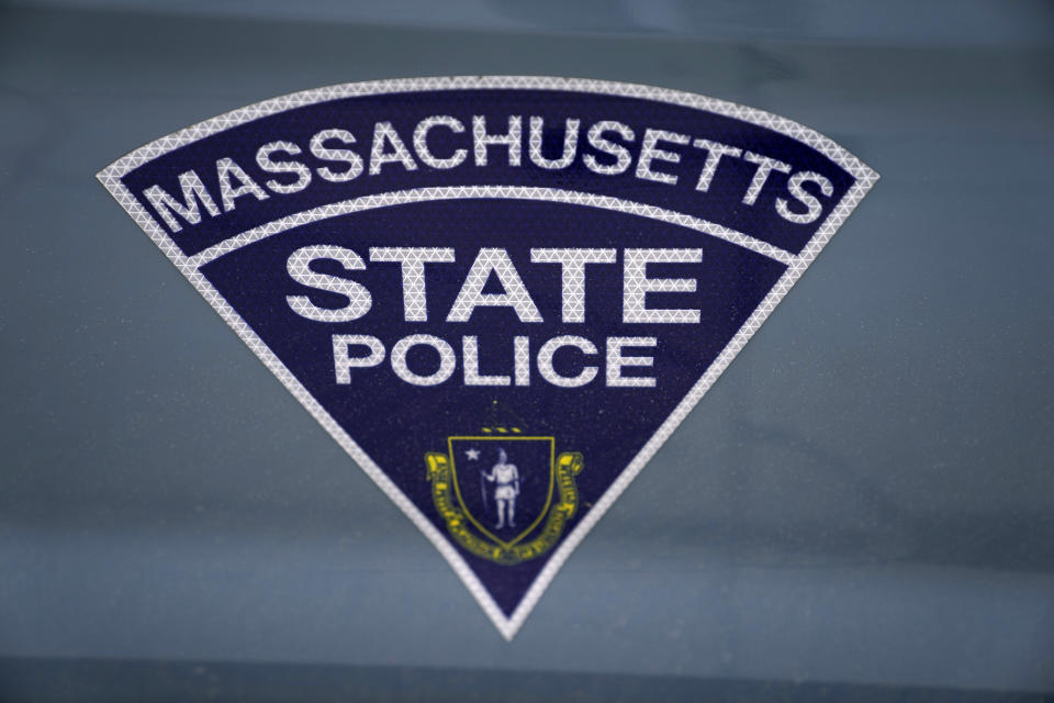 The seal of the Commonwealth of Massachusetts is displayed on a Massachusetts State Police cruiser parked outside the Statehouse, March 3, 2023, in Boston. Two current and two former Massachusetts State Police troopers are among six people charged Tuesday, Jan. 30, 2024 in a scheme to allegedly take bribes including a new snowblower and driveway in exchange for giving passing scores on commercial driving tests, the U.S. attorney’s office said Tuesday. (AP Photo/Charles Krupa, file)