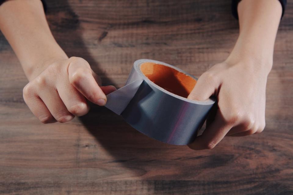 Person holding a roll of duct tape and peeling the end off.