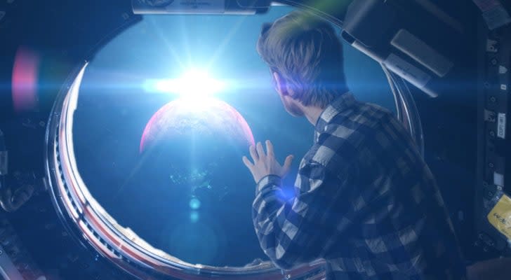 Person looking through space capsule's cabin window into space.