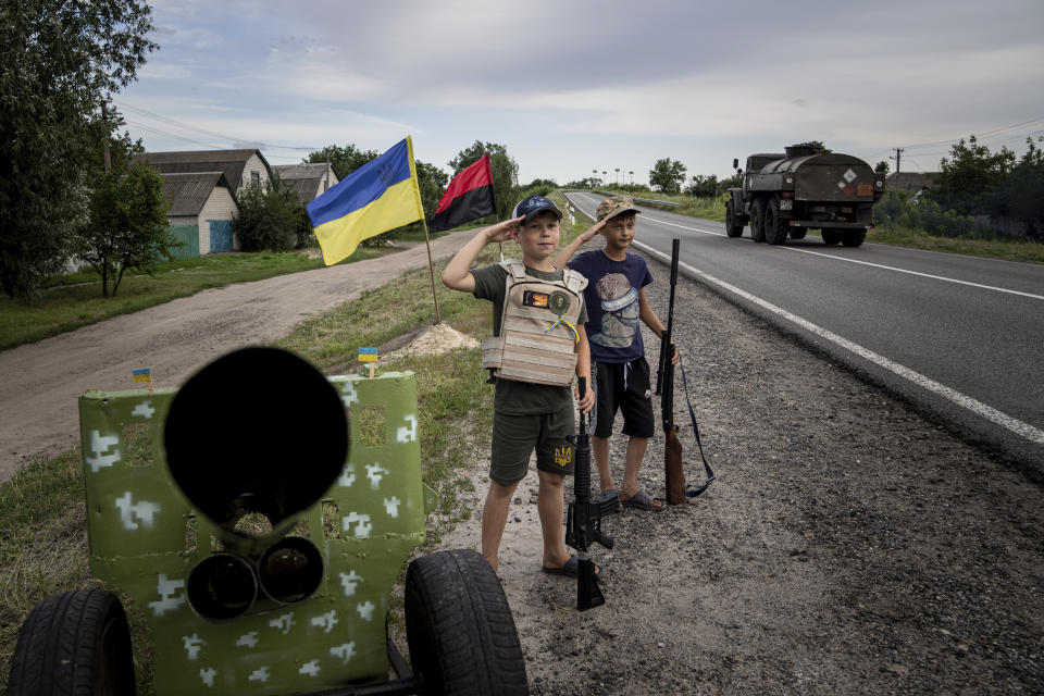 Maksym and Andrii 11, years old boys, salute to Ukrainian soldiers holding plastic guns as they play at the self-made checkpoint on the highway in Kharkiv region, Ukraine, Wednesday, July 20, 2022. (AP Photo/Evgeniy Maloletka)