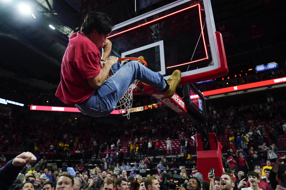 A student climbs a rim as a crowd rushes the court after Maryland defeated Purdue 68-54 during an NCAA college basketball game, Thursday, Feb. 16, 2023, in College Park, Md. (AP Photo/Julio Cortez)