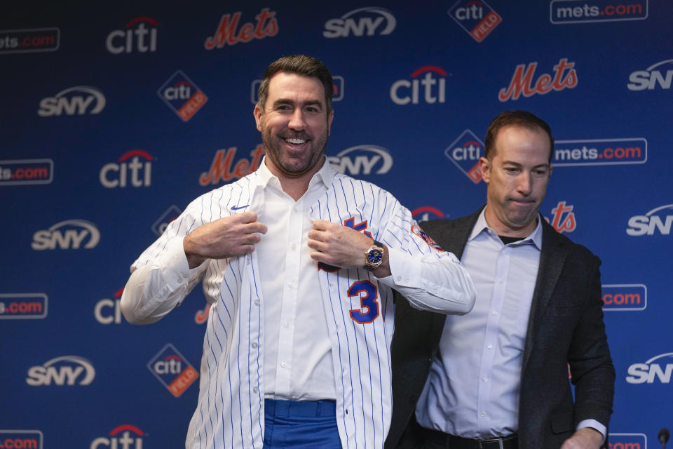 With the help of New York Mets baseball team general manager Billy Eppler, right, pitcher Justin Verlander puts on his new jersey during a news conference at Citi Field, Tuesday, Dec. 20, 2022, in New York. The team introduced Verlander after they agreed to a $86.7 million, two-year contract. It's part of an offseason spending spree in which the Mets have committed $476.7 million on seven free agents. (AP Photo/Seth Wenig)