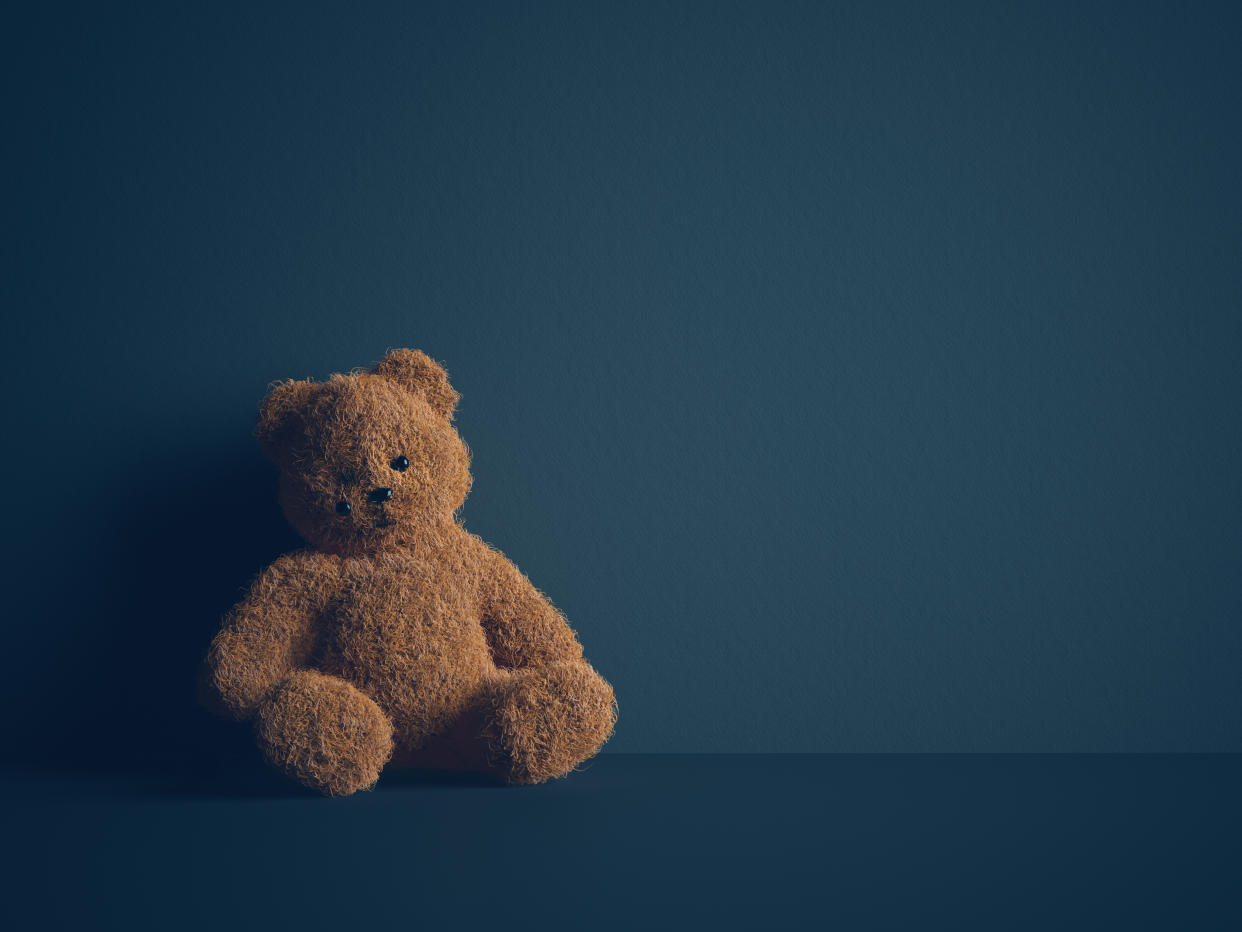 Teddy bear with torn eye sits in dark room. Child abuse and violence concept.