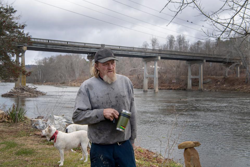 Keith Clemmons stands on his property with his dogs along the French Broad River in Woodfin, December 6, 2023. Clemmons is one of more than 225 residents who have signed a petition in hopes of de-annexing the western part of Woodfin.