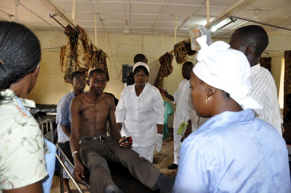 A wounded man, center, is surrounded by medical staff as he arrives for treatment at the Nyanya general hospital following a blast at a bus park in Abuja, Nigeria, Monday, April. 14, 2014. Police say an explosion that ripped through a busy bus station in Nigeria's capital has killed and injured scores of people. (AP Photo/Gbemiga Olamikan)