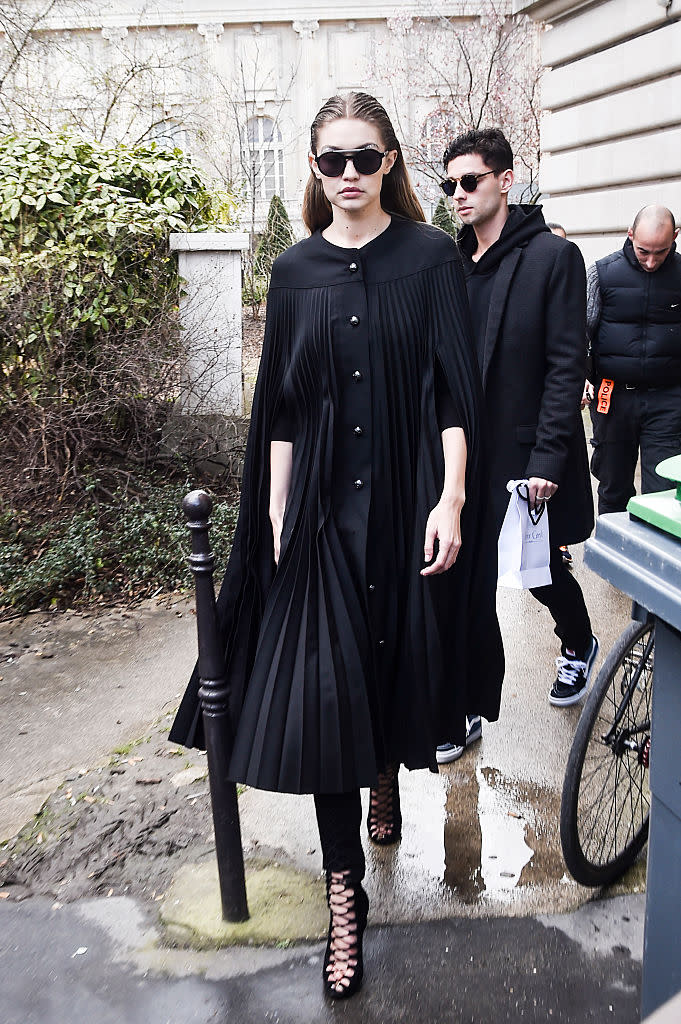 Total look black pour Gigi avec cette cape plissée et boutonnée sur le devant assortie de sandales ouvertes. On dit OUI !