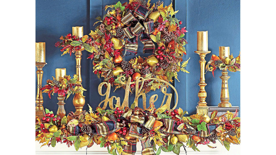 Fall mantel decor ideas: Fireplace mantel decorated with traditional colorful leafy garland and wreath, gold candlesticks and gold 