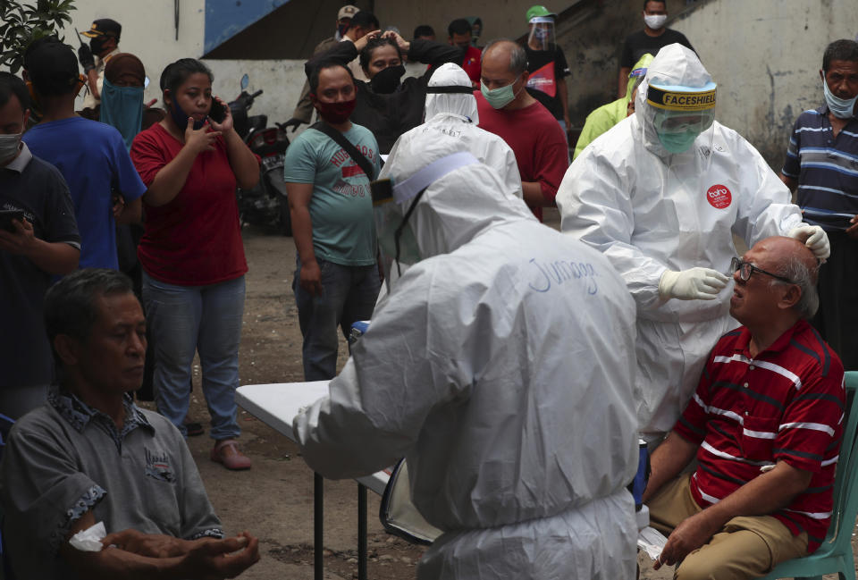 People look on as health workers take nasal swab samples during a mass testing for the coronavirus conducted at a market in Jakarta, Indonesia, Friday, May 29, 2020. (AP Photo/Achmad Ibrahim)