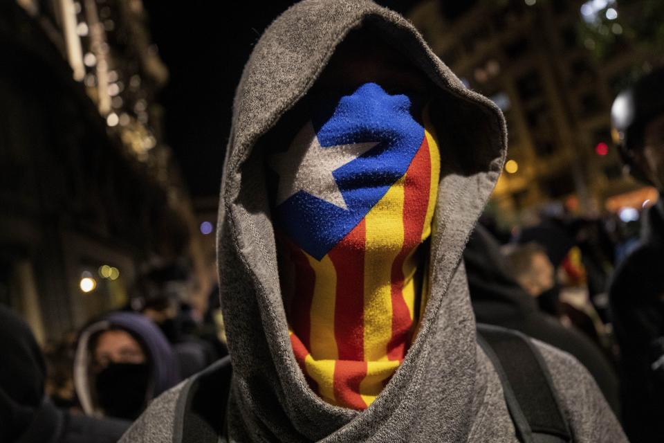FILE - A Catalan pro-independence protestor wearing an Estelada, or Catalan independence mask, stands in front of police, not seen, during a protest in Barcelona, Saturday, Oct. 26, 2019. Thousands of ordinary citizens got into legal trouble for their parts in Catalonia’s illegal independence bid that brought Spain to the brink of rupture six years ago. Now they are hoping to be saved. Spain’s acting prime minister, Pedro Sánchez, is negotiating with Catalan separatist parties on the possibility of issuing a sweeping amnesty for the separatists in exchange for their helping him form a new national government in Madrid. (AP Photo/Bernat Armangue, File)