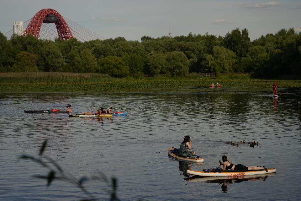 Women sitting on SUP-boards, watch a raft of ducks in Moskva river at Serebryany Bor park in Moscow, Russia, Thursday, July 11, 2024. Warm weather has settled in Moscow with a temperature of 30 Celsius, (86 Fahrenheit) and will increase in the coming days. (AP Photo/Pavel Bednyakov)