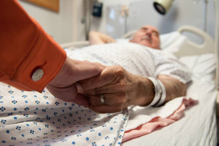 Person holding an elderly patient's hand in a hospital bed, conveying care and support