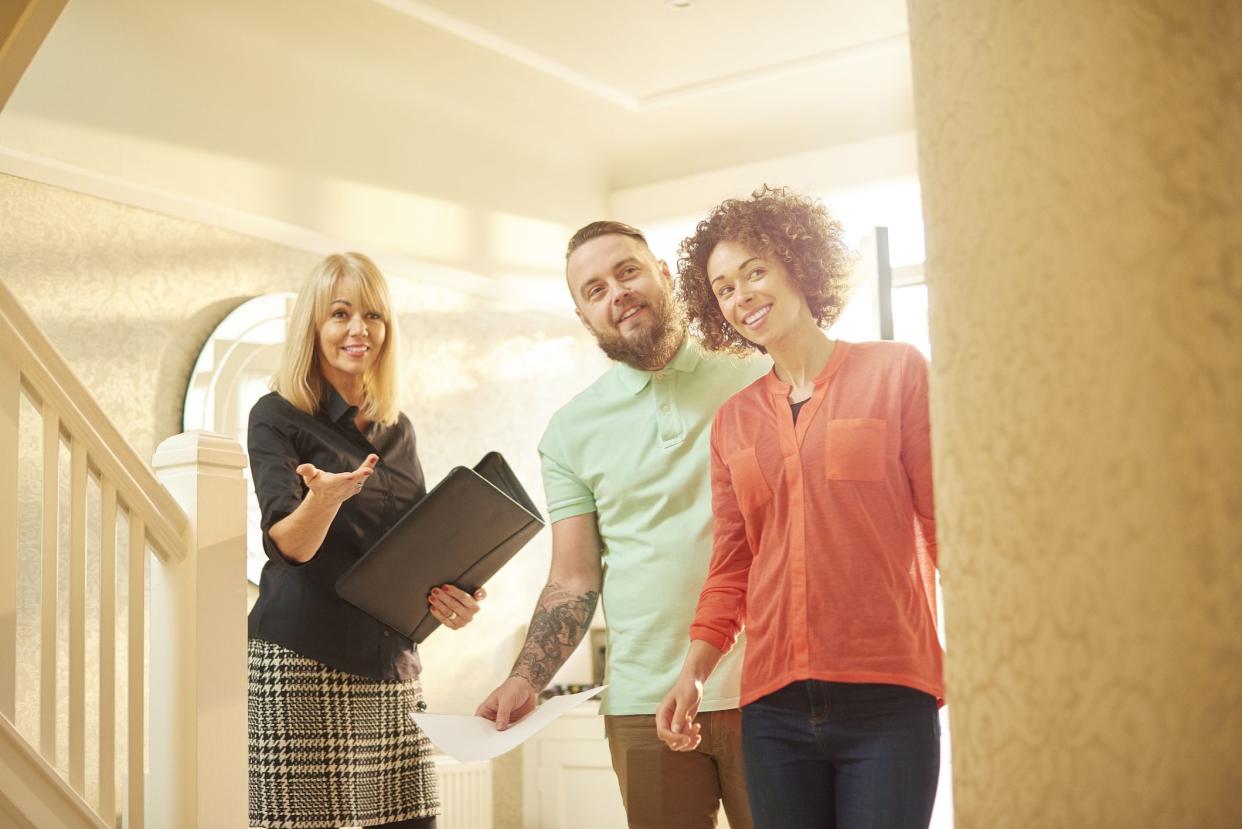 a young couple view a property guided by an estate agent. They are standing in the hallway of house and chatting about the paperwork that they are holding .