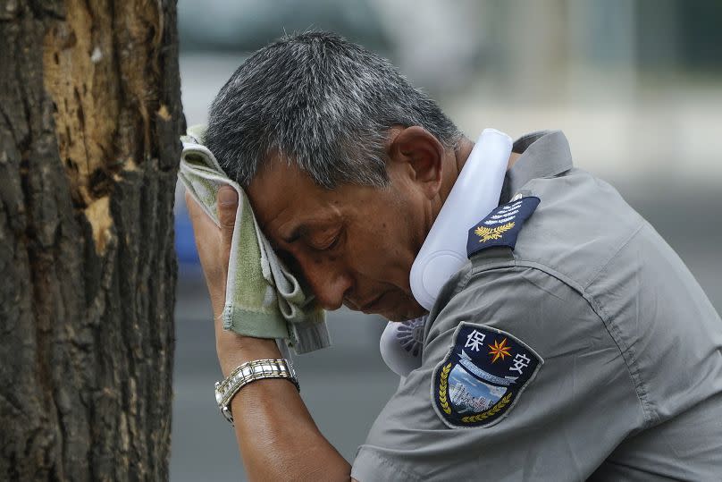 A security guard wearing an electric fan on his neck wipes his sweat on a hot day in Beijing, Monday, July 3, 2023.