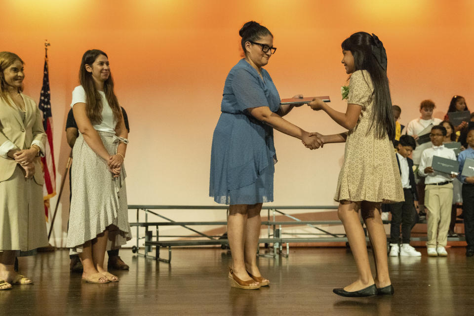 Sophia Prado receives a diploma on the stage during a graduation ceremony at Trevor Day School, Friday, June 21, 2024, in New York. Thousands of migrant families in New York City are facing a summer of uncertainty for their school-aged children with a citywide limit of 60 days in a shelter before needing to reapply or find their own. (AP Photo/Jeenah Moon)