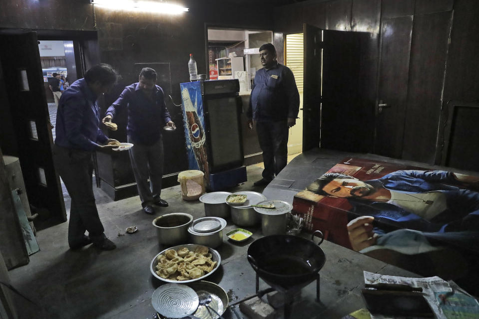 In this Thursday, March 30, 2017 photo, employees eat lunch together next to a Bollywood film poster at Regal Theater in New Delhi, India. From Bollywood superstars to political heavyweights, the theater had hosted some of India’s biggest names over more than eight decades. But with nostalgic theater-goers singing their way to the exits after a final showing of a Bollywood classic, the iconic New Delhi theater has closed its doors to make way for a multiplex. (AP Photo/Manish Swarup)