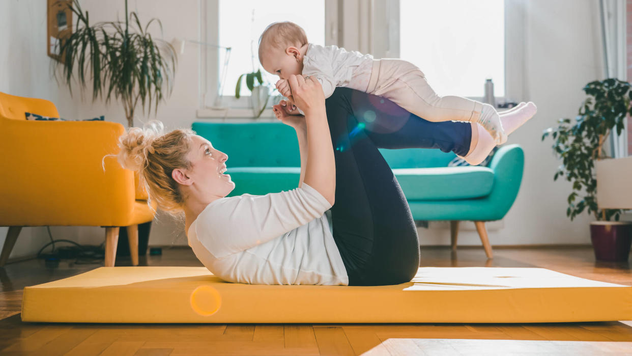 Mother Exercise With Her Baby on yellow mat At Home.