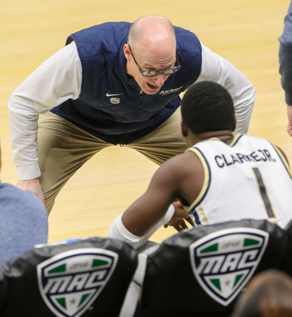 Akron coach John Groce talks with Garvin Clarke on the bench during the Zips' game against Buffalo in a MAC quarterfinal Thursday at Rocket Mortgage Fieldhouse.