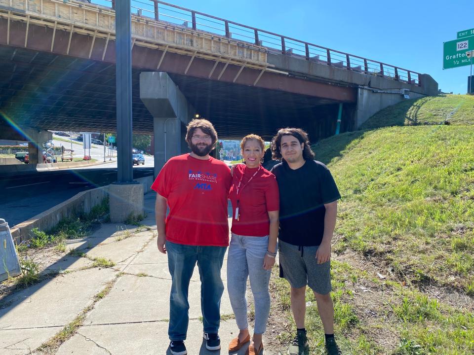 From right, Brian Mulhearn, Nelly Medina and Andy Saltzberg stand in front of the bridge passing over East Central Street, advocating for the passage of Question 1 this fall.