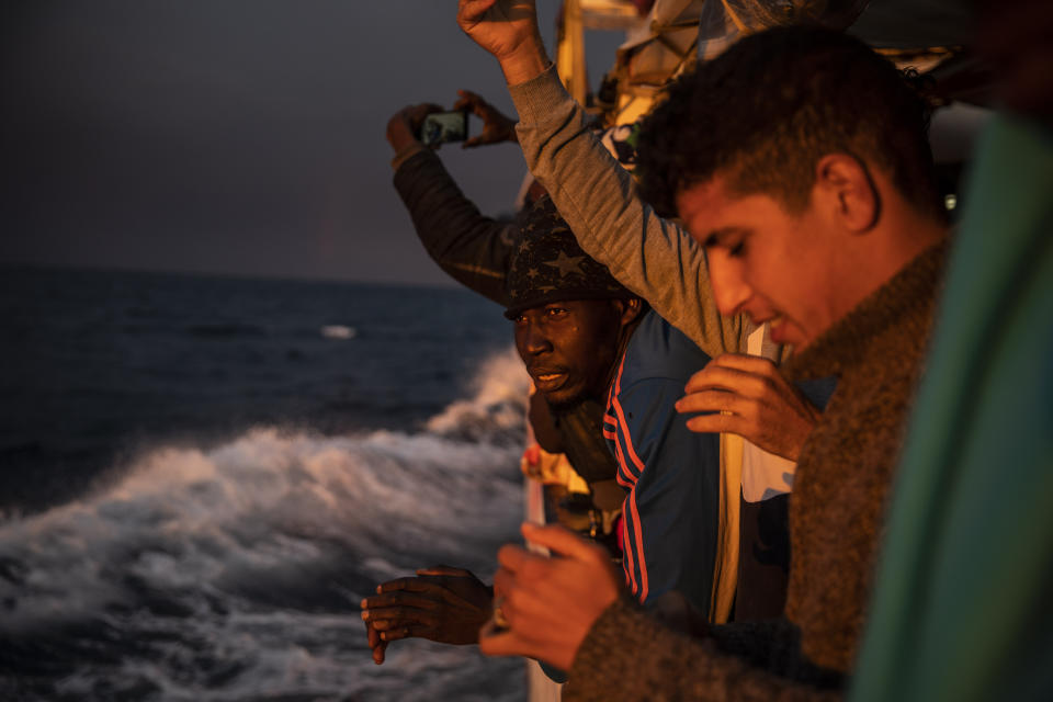 FILE - In this Sunday Jan. 12, 2020 file photo, men from Nigeria and Morocco watch the sunset aboard the Open Arms rescue vessel as the ship sails north with 118 people from different nationalities who were rescued on Friday off the Libyan coast. The European Union announced Tuesday, March 31, 2020 the launch of a new naval mission in the Mediterranean Sea aimed at enforcing the U.N arms embargo on Libya, after Italy blocked a previous operation claiming that the warships attracted migrants. (AP Photo/Santi Palacios, File)