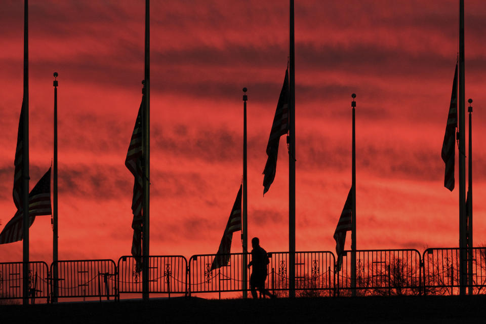A solitary runner passes under the flags hanging at half-staff surrounding the Washington Monument at day break in Washington, Wednesday, Feb. 24, 2021. President Joe Biden ordered the flags to be lowered in honor of the 500,000 lives lost to COVID-19 in the U.S. (AP Photo/J. David Ake)