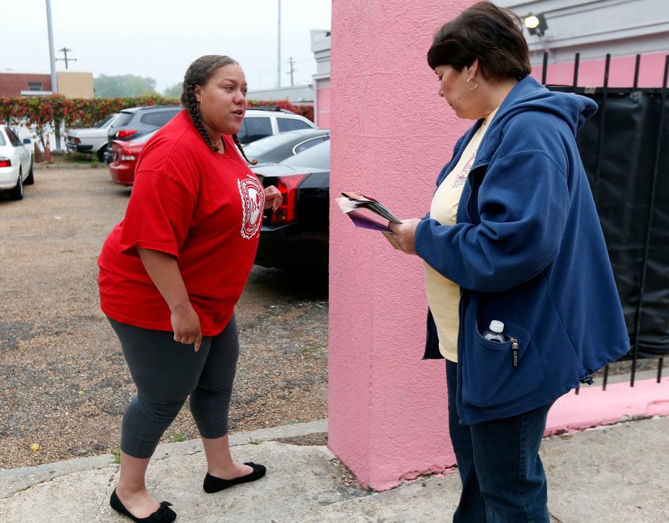 A woman approaches another women at the entrance to a parking lot.