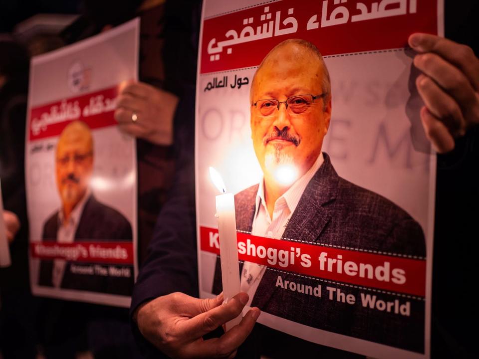 Two people holding candles and posters of the Saudi journalist Jamal Khashoggi.