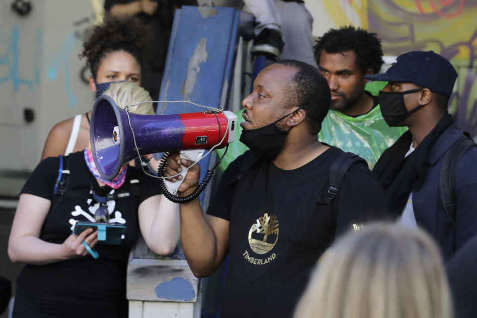 Mark Henry Jr., center, a Black Lives Matter leader, speaks into a megaphone in a doorway of the Seattle Police Department East Precinct building, which has been boarded up and abandoned except for a few officers inside, Thursday, June 11, 2020, in Seattle. The building is located in what is being called the "Capitol Hill Autonomous Zone." Following days of violent confrontations with protesters, police have largely withdrawn from the neighborhood. (AP Photo/Ted S. Warren)