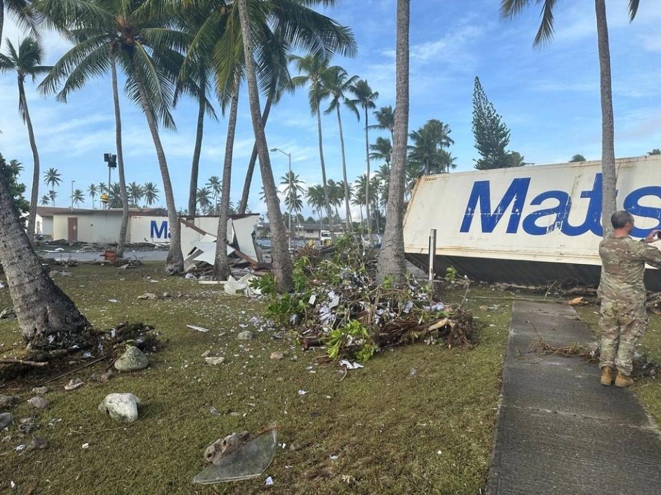 debris is seen at the base of palm trees as a soldier takes a photo of the damage