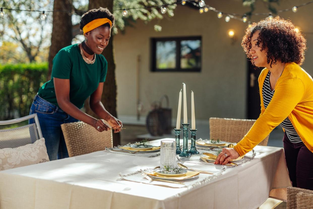 Two women preparing table for dinner party in the backyard