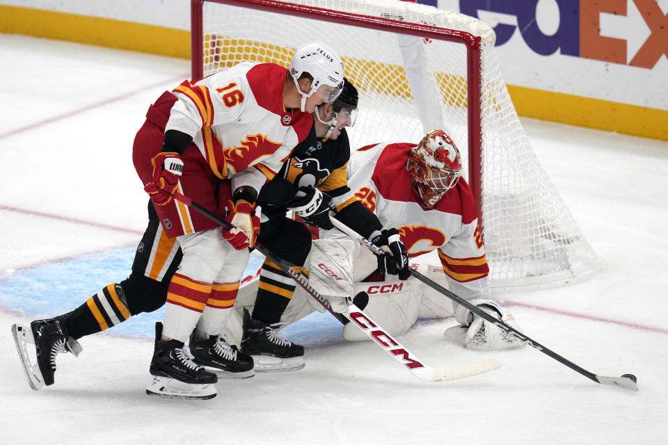 Pittsburgh Penguins' Drew O'Connor, center, can't get his stick on the puck in front of Calgary Flames goaltender Jacob Markstrom (25) with Nikita Zadorov (16) defending during the first period of an NHL hockey game in Pittsburgh, Saturday, Oct. 14, 2023. (AP Photo/Gene J. Puskar)