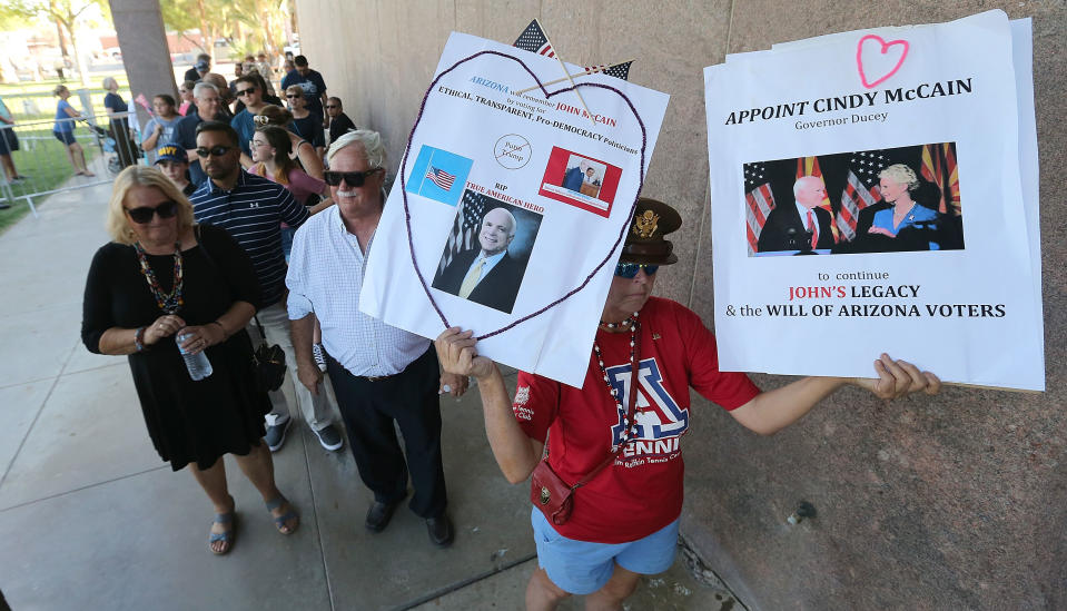 <p>Cindy O’Neil of Tucson, Arizona (R) holds up signs as she and others wait in line for the public viewing of the late Sen. John McCain as his body lies in state at the Arizona State Capitol Rotunda on Aug. 29, 2018 in Phoenix, Ariz. (Photo: Ralph Freso/Getty Images) </p>