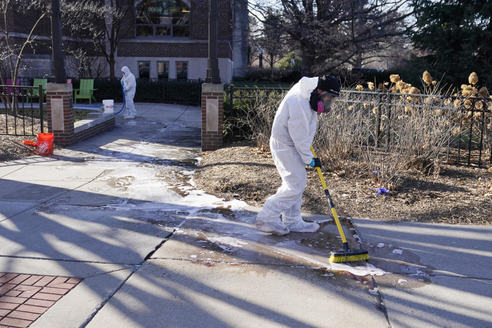 Workers dressed in white protective gear clean up outside the scene of a deadly shooting on MSU’s campus.