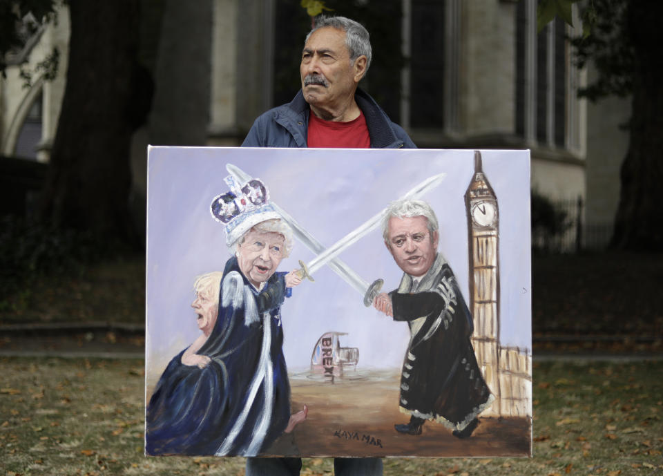 Political artist Kaya Mar holds his painting of British Prime Minister Boris Johnson, left, Britain's Queen Elizabeth II, center, and Speaker of the House of Commons John Bercow as he stands opposite Parliament Square in London, Tuesday, Sept. 3, 2019. Opposition parties are challenging British Prime Minister Boris Johnson's insistence that the U.K. will leave the EU on Oct. 31, 2019 even without a deal, setting up a pivotal day in British politics. (AP Photo/Matt Dunham)