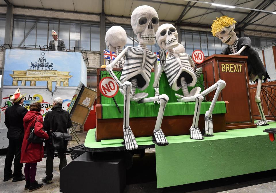 A satiric carnival float depicting the Brexit and British members of Parliament as skeletons, is watched by revellers during a preview in a hall in Cologne, Germany, Tuesday, Feb. 18, 2020. The traditional carnival parades on Rosemonday make fun of politics and are watched by hundreds of thousands in the streets of Cologne, Duesseldorf and Mainz. (AP Photo/Martin Meissner)