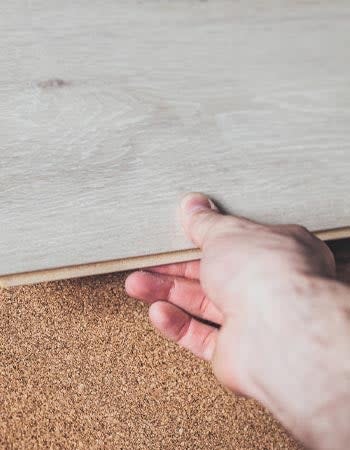 A close up of a person's hand laying down grey flooring.