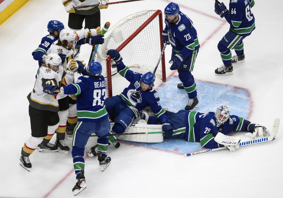 Vancouver Canucks' Troy Stecher (51) falls on goalie Jacob Markstrom (25) as there is a scramble at the net against the Vegas Golden Knights during the second period of an NHL Western Conference Stanley Cup playoff game, Sunday, Aug. 30, 2020, in Edmonton, Alberta. (Jason Franson/The Canadian Press via AP)