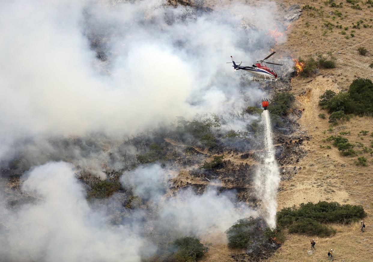 Firefighters battle a wildfire from the ground as a helicopter drops water above them in Springville, Utah, on Monday.
