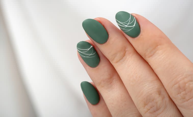 hands of a young woman with green olive matte nails on a light gray