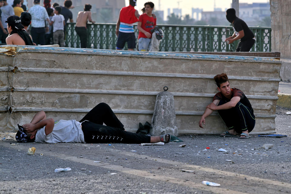 Anti-government protesters take cover while security forces use tear gas to disperse them, on the closed Sinak Bridge that leads to the Green Zone government areas in Baghdad, Iraq, Sunday, Oct. 25, 2020. Thousands of Iraqi protesters have taken to the streets to mark one year since mass anti-government demonstrations swept Baghdad and Iraq's south. Protesters marched Sunday in the capital and several southern cities to renew demands to bring an end to corruption perpetuated by Iraq's politicians. (AP Photo/Khalid Mohammed)