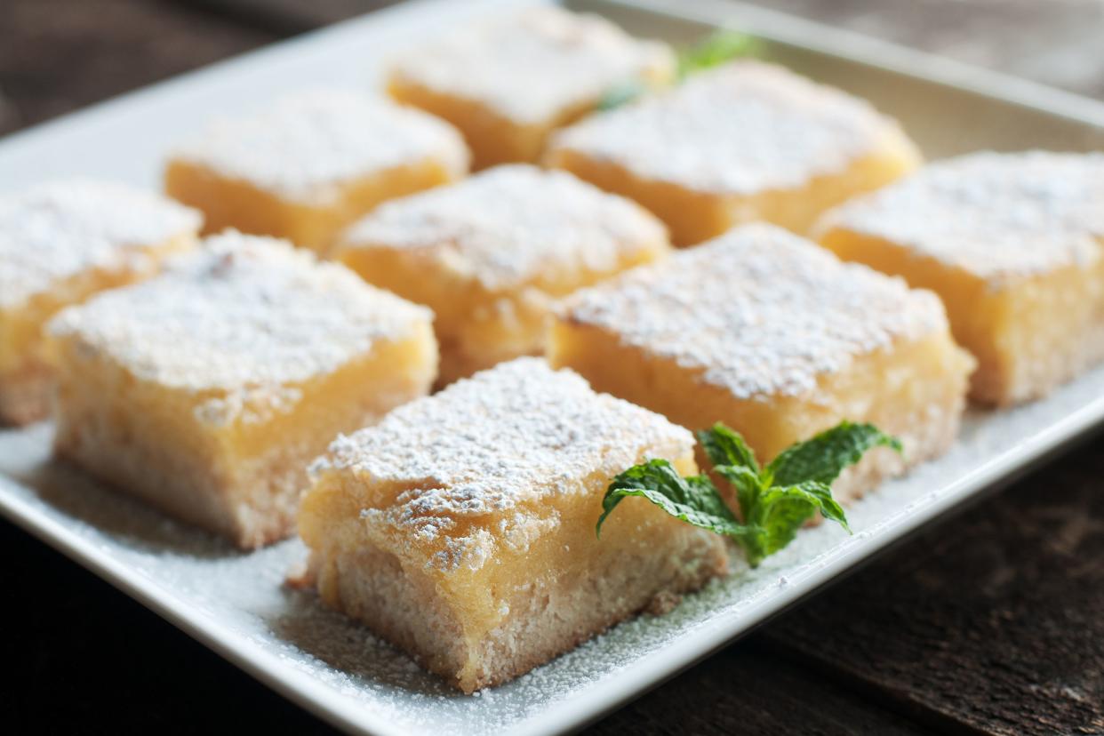 Closeup of nine lemon squares with powdered sugar on a square white plate with a blurred background